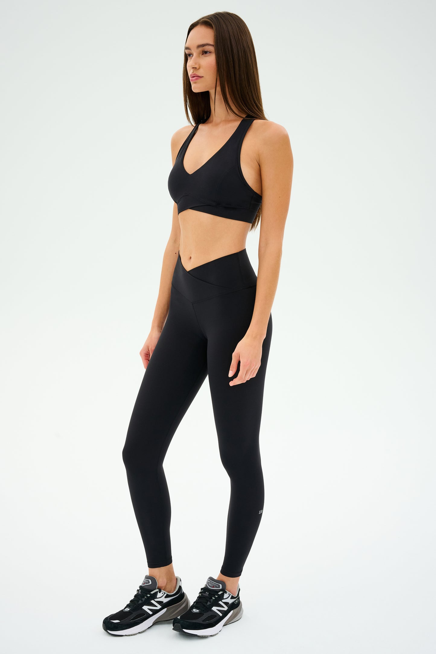 A person showcases the multi-sport performance of the ultra-luxe fabric by wearing a black Mia Rigor Bra from SPLITS59, paired with black leggings and athletic shoes, against a white background.