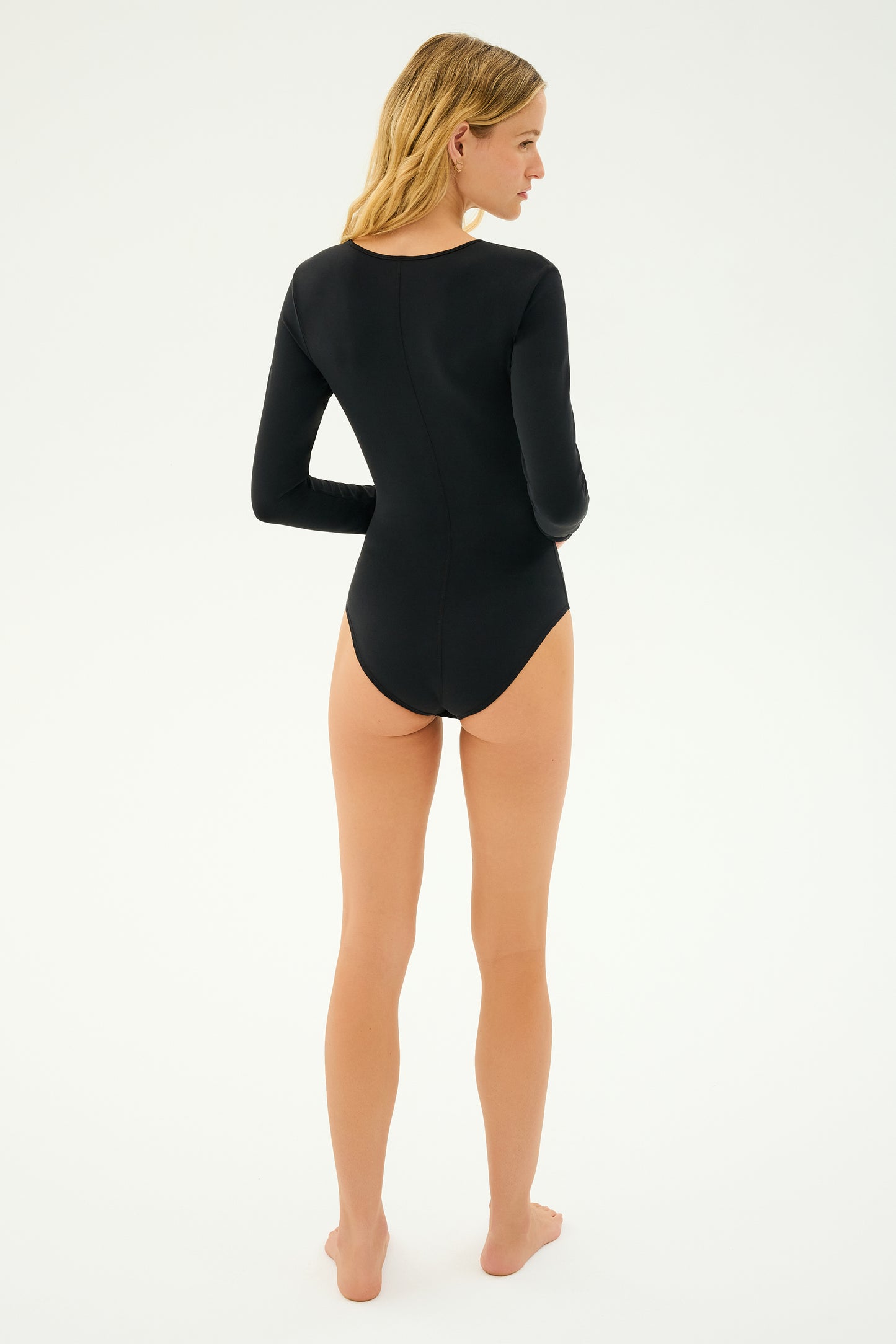 A woman wearing the SPLITS59 Airweight Scoop Neck Bodysuit in black stands barefoot on a plain background, facing away.