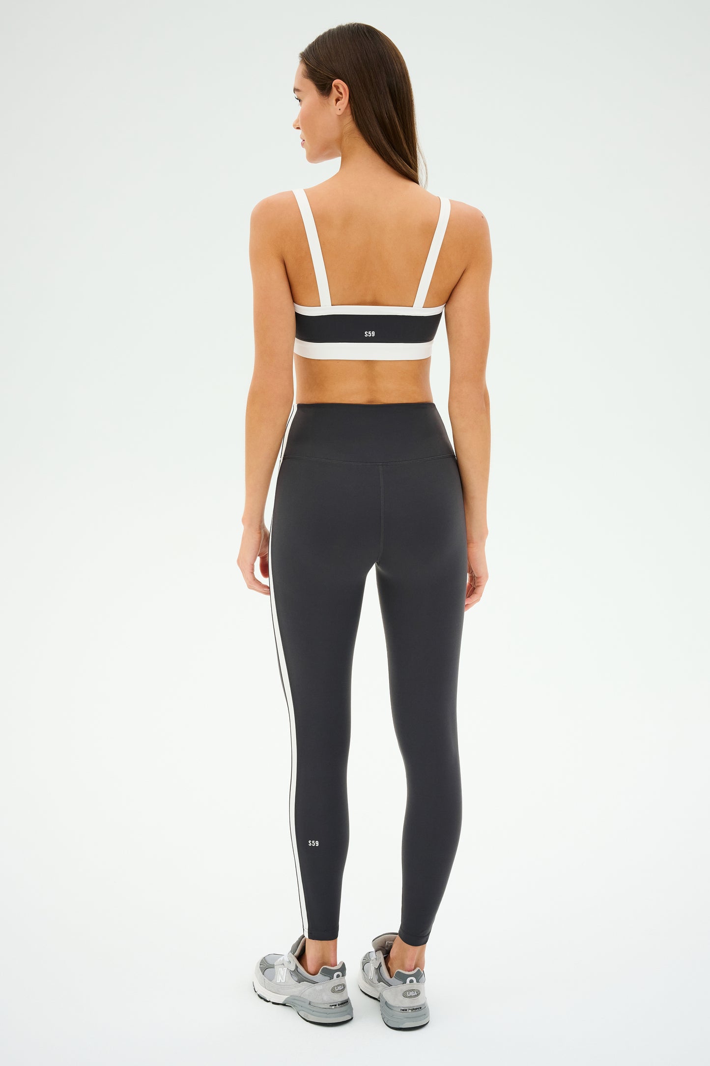 A person in black and white athletic wear displays the SPLITS59 Clare High Waist Rigor 7/8 leggings in Graphite/White, crafted from high-performance Rigor fabric, ideal for gym workouts, against a light background.