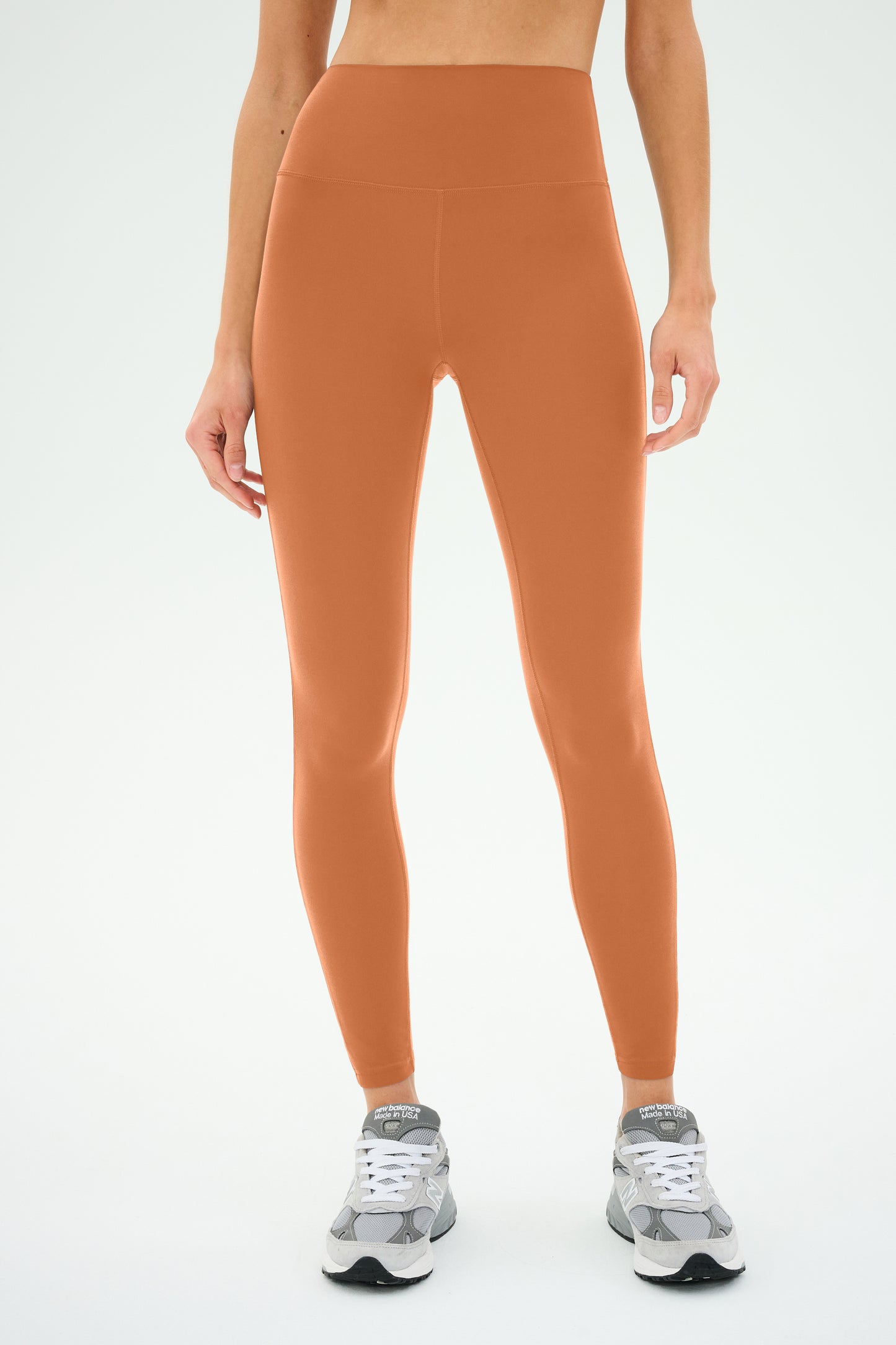 A person wearing Clare High Waist Rigor 7/8 leggings in Pecan/White by SPLITS59 and gray sneakers stands on a white background.