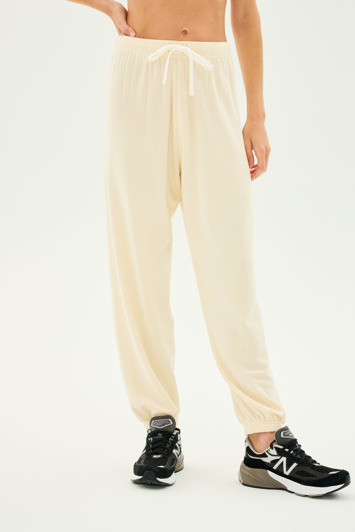 A person wearing the Andie Oversized Fleece Sweatpant in Creme by SPLITS59, ideal for workouts, paired with black sneakers against a white background. Made in Los Angeles.