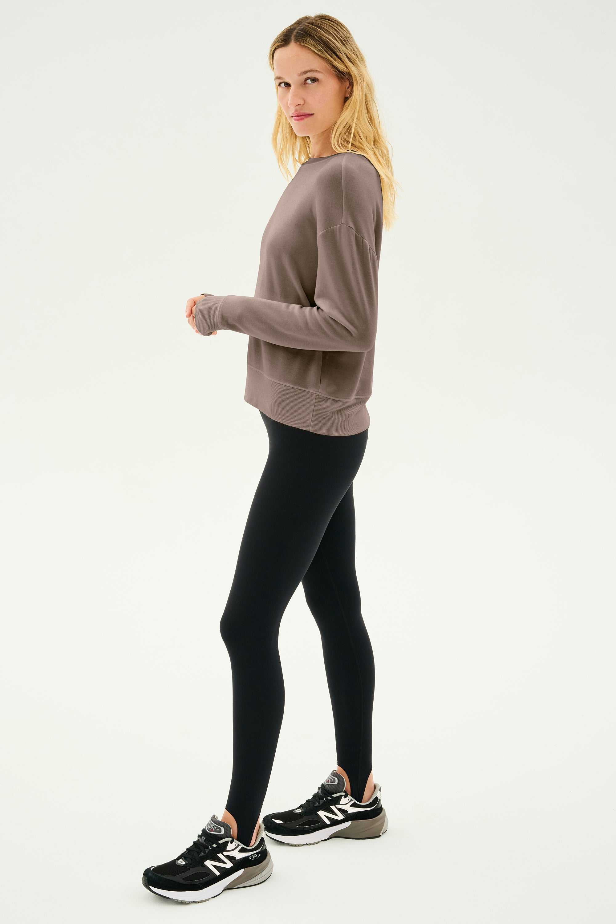 An individual wearing the Sonja Fleece Sweatshirt in Lentil by SPLITS59 teams it with black leggings and sneakers, standing against a plain white background.