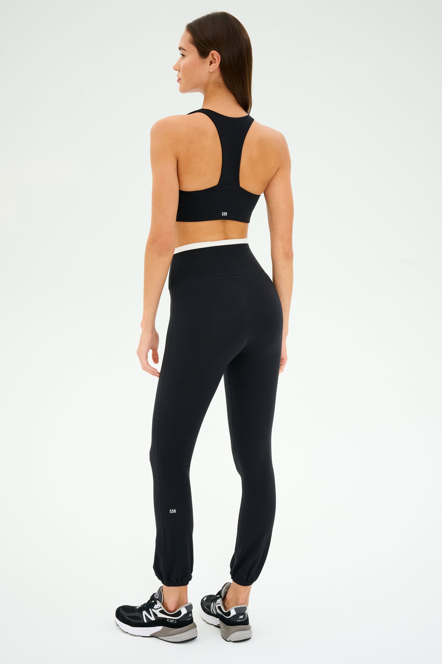 A person in SPLITS59's Icon Dual High Waist Airweight Legging in black stands against a light background, showcasing the luxe High Waist design.