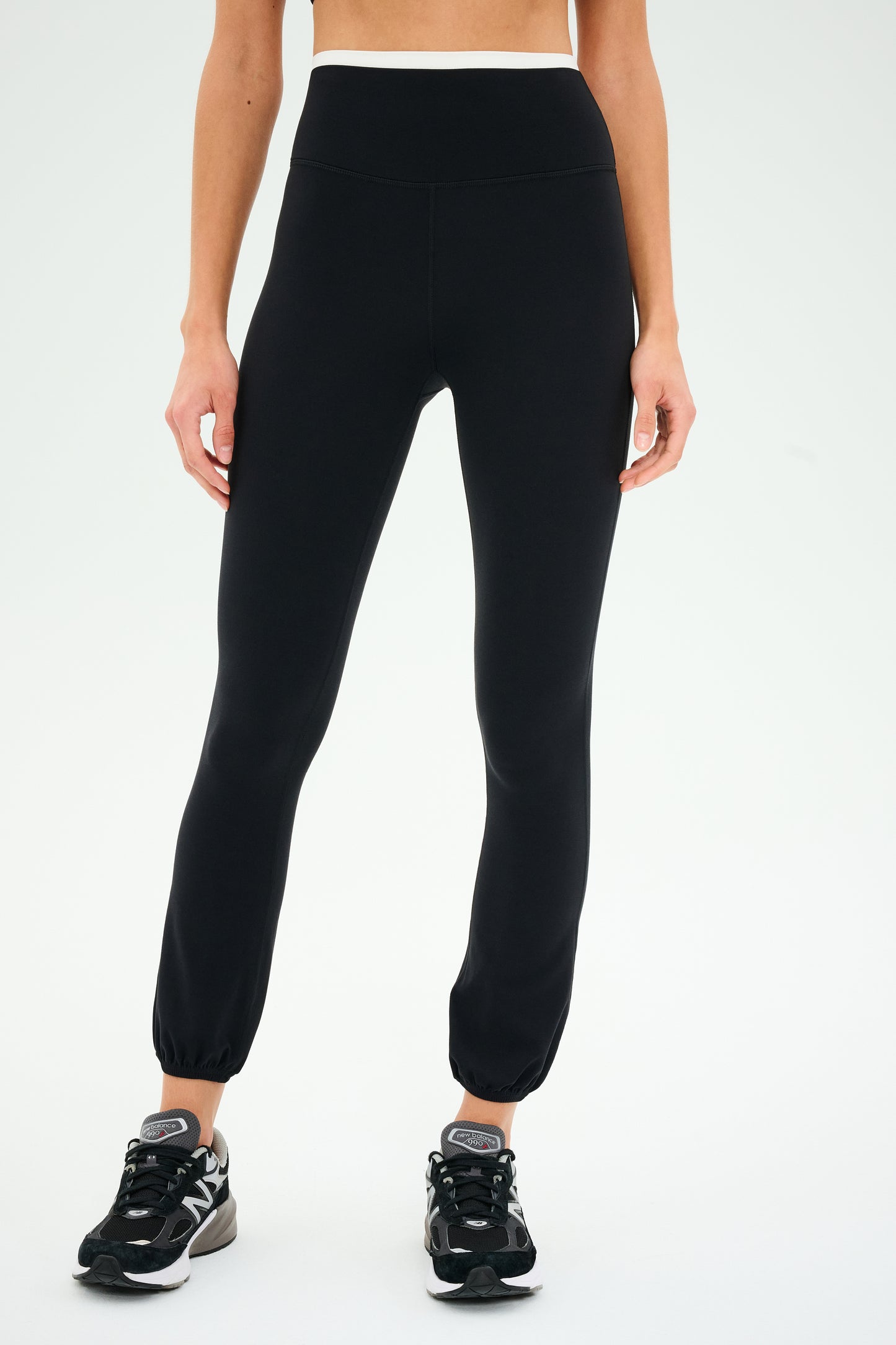 A person in Icon Dual High Waist Airweight Legging by SPLITS59 and black sneakers stands against a white background.