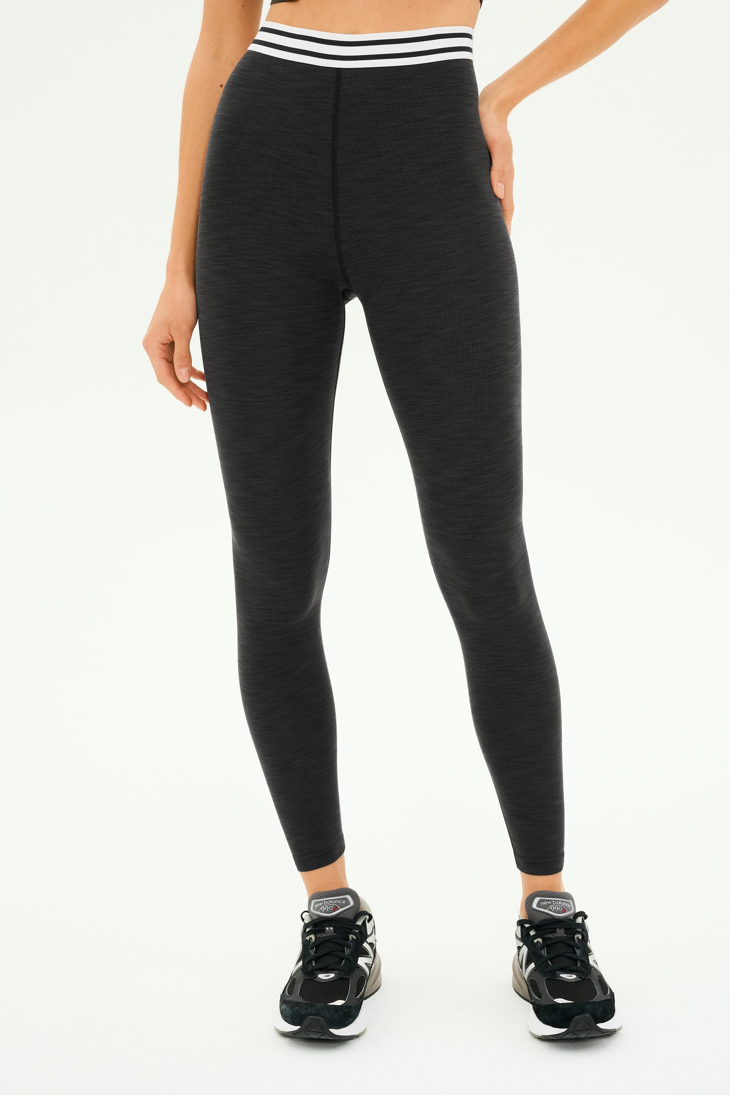 A person is wearing the Bailey Active Rib High Waist 7/8 in Heather Graphite by SPLITS59, featuring a striped waistband, perfectly teamed with black sneakers for gym workouts.