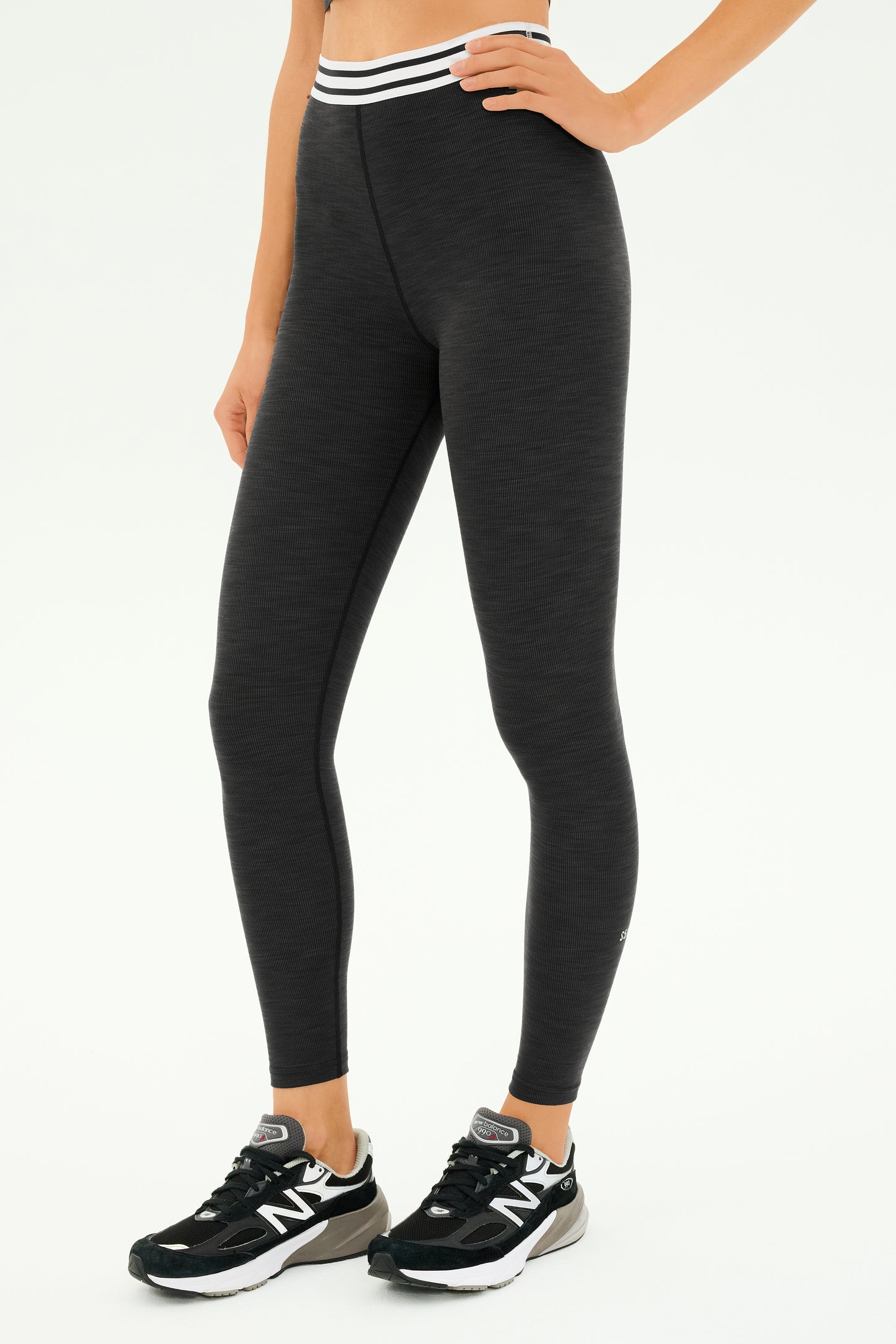 A person wearing the SPLITS59 Bailey Active Rib High Waist 7/8 in Heather Graphite and black sneakers stands against a plain background, ready for gym workouts.