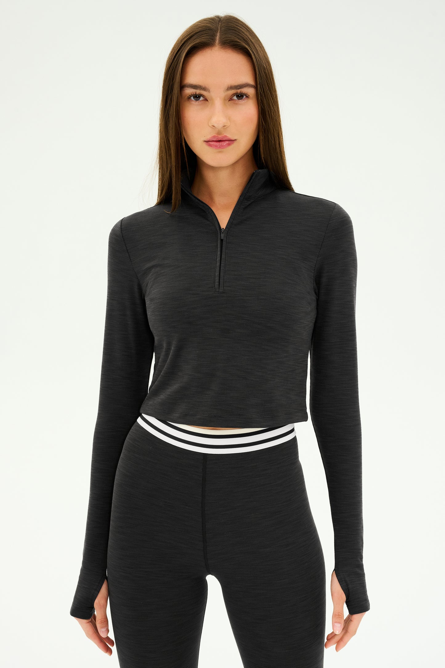 Dressed in the Stevie Active Rib Half Zip - Heather Graphite from SPLITS59, a person stands against a plain background. With its half-zip pullover and active rib fabric leggings, they're ready for their gym workouts.