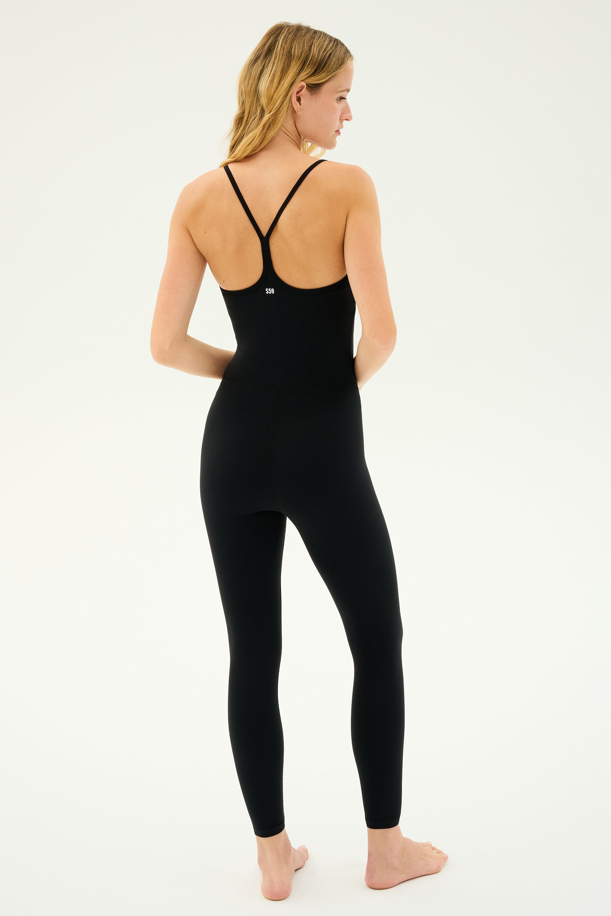 A person stands barefoot with their back to the camera, wearing the SPLITS59 Airweight Jumpsuit in black.