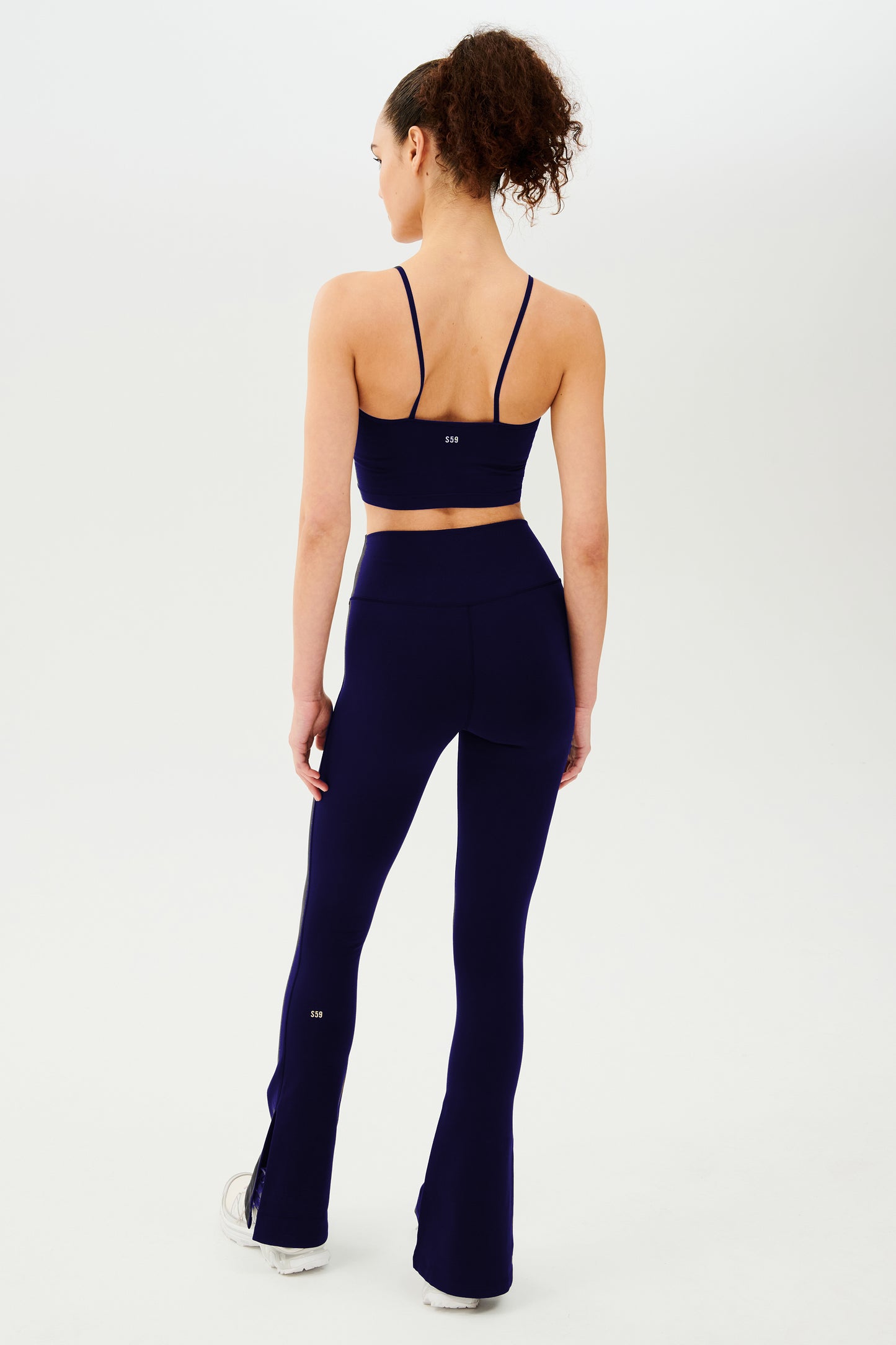 The back view of a woman in navy, SPLITS59 Raquel High Waist Flare w/ Split Hem - Indigo leggings.