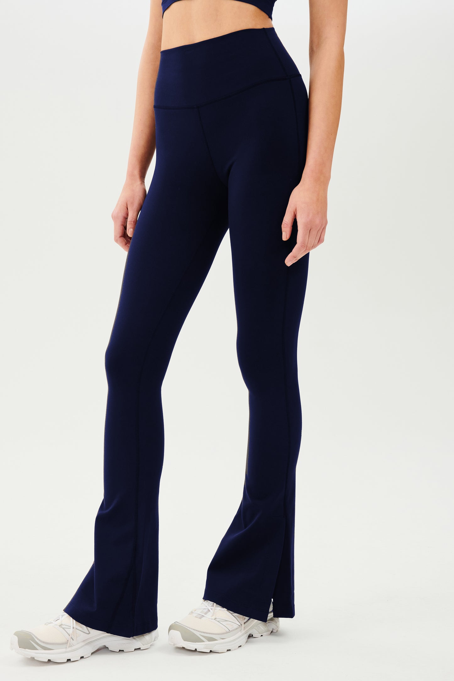 A woman wearing SPLITS59 Raquel High Waist Flare w/ Split Hem - Indigo leggings and a crop top.